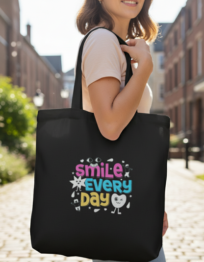 Person holding a black tote bag with 'Smile Every Day' text and smiley face design.